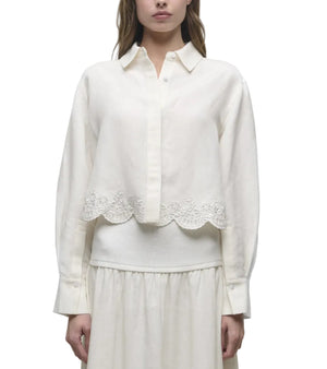 A woman wears the Simkhai Ames Linen Shirt, an off-white linen-blend long-sleeve button-up blouse with an embroidered floral hem, paired with a matching skirt.