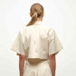 A person with straight, light brown hair in a low ponytail is shown from behind, wearing the Simkhai Blair Shirt in light beige with short sleeves and a matching skirt.