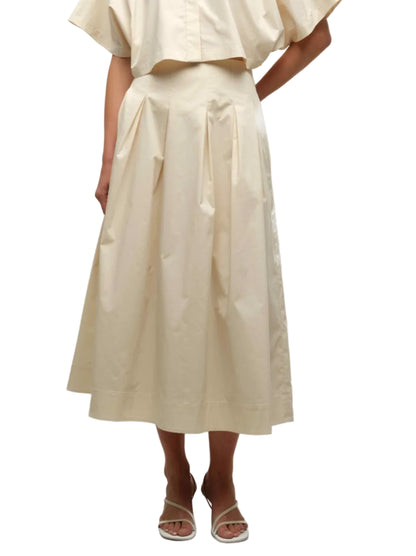 Someone is wearing the Simkhai Elora Midi Skirt, a cream-colored, high-waisted pleated skirt, paired with a matching short-sleeve top and white heeled sandals.