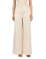 A person wears the Simkhai Leroy Pleated Wide Leg Pant—high-waisted beige trousers with front pleats and belt loops—paired with open-toe sandals.
