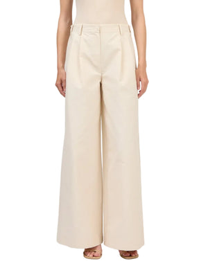 A person wears the Simkhai Leroy Pleated Wide Leg Pant—high-waisted beige trousers with front pleats and belt loops—paired with open-toe sandals.