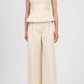 A person wearing Simkhai's Leroy Pleated Wide Leg Pant paired with a sleeveless, cream peplum top and open-toe sandals, standing against a plain background.