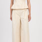 A person wears the Simkhai April Bustier Top, a sleeveless fitted beige peplum top, paired with matching wide-leg pants and open-toe heels, standing against a plain background.
