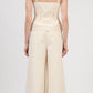 A person with a single braid is shown from the back, wearing the Simkhai April Bustier Top in beige with wide straps, paired with matching high-waisted, wide-leg pants.