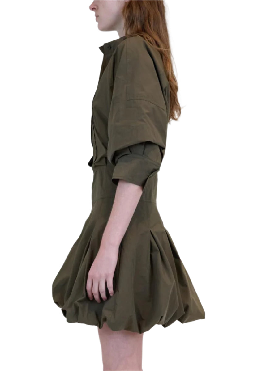 A person in a side profile wears the Simkhai Effie Bubble Mini Dress in olive green cotton poplin, featuring puffed sleeves and a bubble skirt, set against a white background.