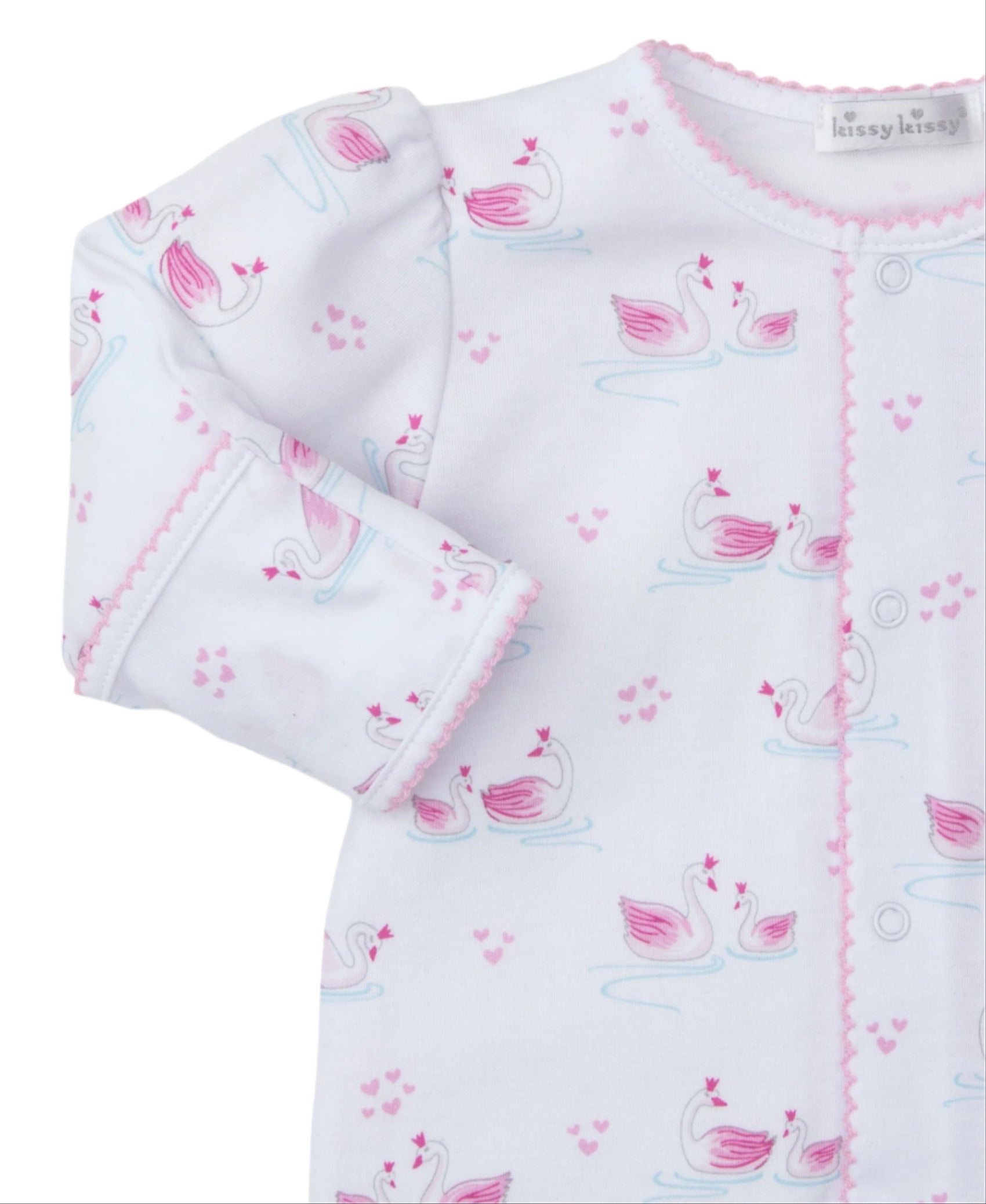 The Kissy Kissy Swan Sanctuary Footie is a white onesie made from soft Pima cotton, featuring pink trim and a charming swan pattern with heart designs in pink and blue shades.