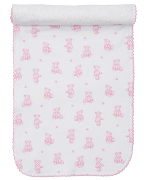 A white Pima cotton baby blanket with pink teddy bears, flowers, and pink scalloped trim, partially rolled at the top. Coordinates perfectly with Kissy Kissy’s Teddy Bear Time Burp Cloth for a charming matching set.