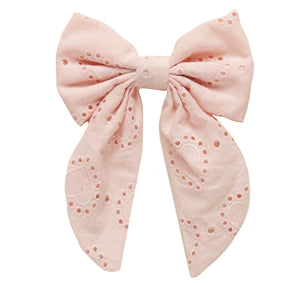 The Noralee Everly Bow by Noralee showcases pink heart eyelet fabric with large loops and long tails, elegantly fastened with a rose gold alligator clip.