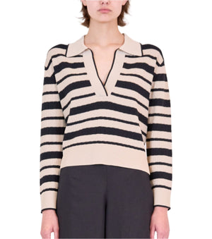 A person wearing the Simkhai Miller Polo, a beige and black horizontal striped collared V-neck sweater, paired with black pants.