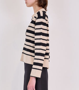 A person in profile wears the Simkhai Miller Polo, a beige and black striped long-sleeve sweater, paired with a black skirt against a plain background.