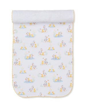 Introducing the Duck Pond Paddles Burp Cloth by Kissy Kissy—a white Pima cotton cloth edged in yellow, adorned with a charming repeating print of ducks and ducklings among ponds and grass. Soft and comfortable, it is rolled at the top and displayed flat on a white background, making it ideal for gentle burping or as a cozy companion to your favorite baby blankets.