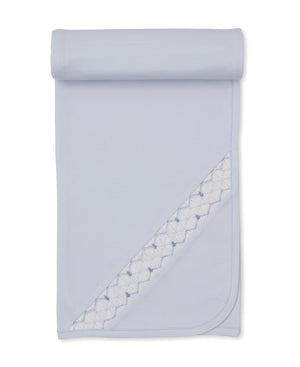 Hand Smocked Blanket by Kissy Kissy in light blue Pima cotton, featuring decorative stitched trim, shown partially unrolled on a white background.