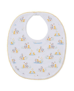 The Duck Pond Paddles Bib by Kissy Kissy is a white baby bib with yellow scalloped trim, crafted from the softest Pima cotton for ultimate comfort and adorned with a playful duck and duckling print among grass and water scenes.