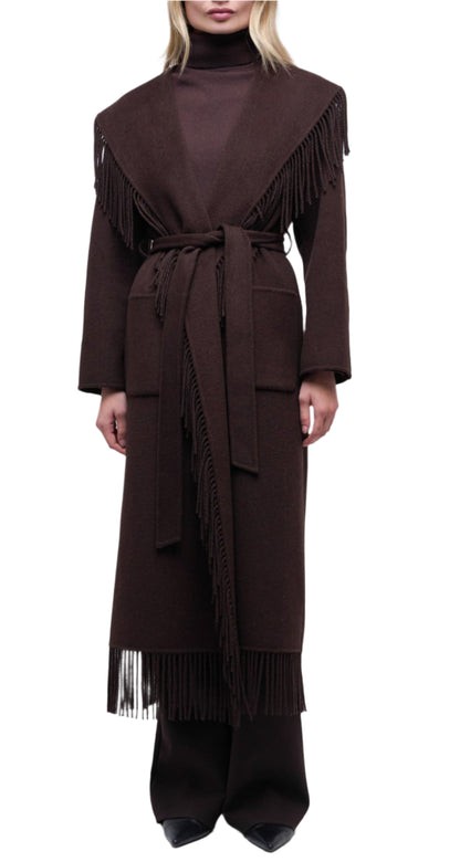A person wearing the Simkhai Carrie Fringe Robe Coat—a long, dark brown shawl-collar style with a self-tie belt and fringed hem—over a matching turtleneck and wide-leg pants, standing against a white background.