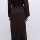 A person is seen from the back wearing the Simkhai Carrie Fringe Robe Coat, a long brown coat with a fringed hem and shoulder fringe details, set against a plain white background.
