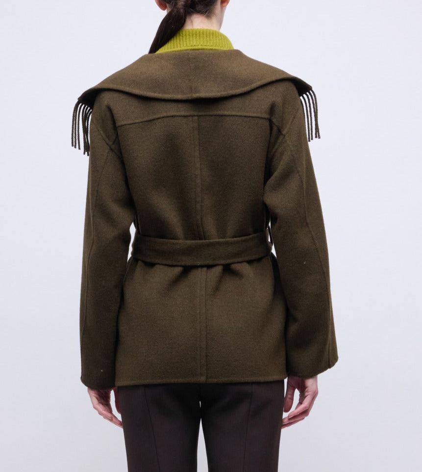 A person is shown from the back against a plain background wearing the Simkhai Rowen Fringe Jacket, a Western-inspired olive green coat featuring a belted waist, wide collar, and fringe detailing.