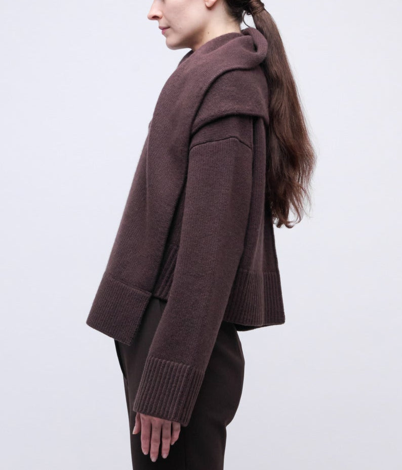 A woman with long brown hair, seen from the side, wears the Simkhai Elson Scarf Sweater and matching brown pants against a plain light background.