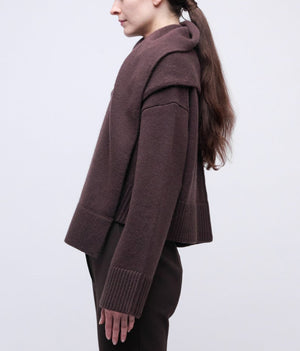 A woman with long brown hair, seen from the side, wears the Simkhai Elson Scarf Sweater and matching brown pants against a plain light background.