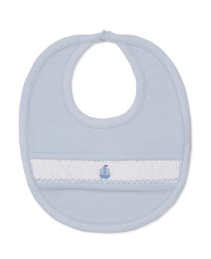 The CLB Summer Medley Smocked Bib by Kissy Kissy is a light blue baby bib made from soft Pima cotton, featuring a hand-smocked white band with a delicate sailboat embroidery at the center and finished with a secure button closure at the neck.