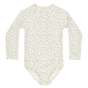 The Rylee & Cru Girls' Delphine Rashguard features long sleeves, a cream base with light green and yellow floral print, and provides sun protection for your little one. Shown laid flat on a white background.