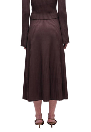 A person wearing Simkhai's Chiara Midi Skirt and a matching long-sleeve ribbed brown top, seen from the back with brown heeled shoes.