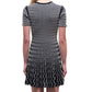 A person with long blonde hair is seen from the back wearing the Simkhai Baylor Mini Dress—a short-sleeve mini dress with a flared skirt and white wavy line pattern.