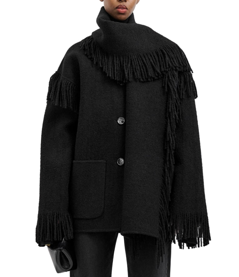 A person wears Toteme's Fringed Scarf Jacket—a black wool-blend bouclé coat with oversized fit, large buttons, and fringe details on the sleeves, hem, and scarf—paired with a small black clutch.