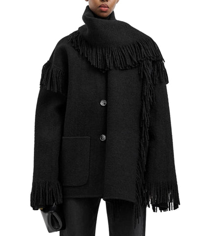 A person wears Toteme's Fringed Scarf Jacket—a black wool-blend bouclé coat with oversized fit, large buttons, and fringe details on the sleeves, hem, and scarf—paired with a small black clutch.