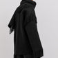 Person wearing Toteme's Fringed Scarf Jacket, a black wool-blend bouclé coat with fringe on the sleeves, back, and hem, featuring an oversized silhouette against a plain light background.