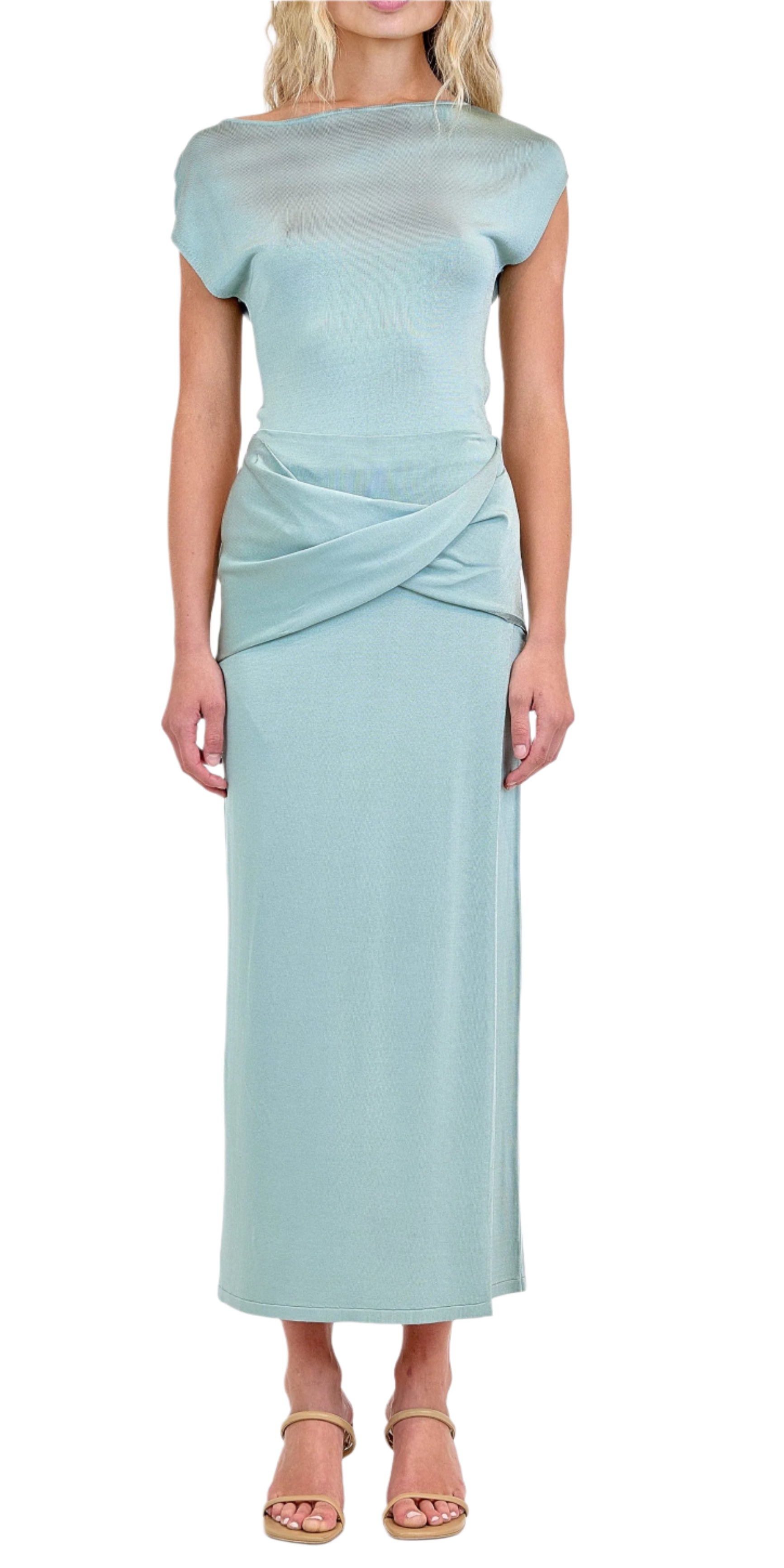 A woman wears the Simkhai Vienna Midi Skirt—a light blue, soft drape, figure-flattering piece—paired with beige sandals, standing against a white background.