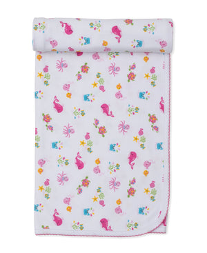 The Kissy Kissy Ocean Antics Blanket is a folded white baby blanket with a charming pink scalloped edge, adorned with a colorful undersea print featuring cartoon whales, octopuses, turtles, fish, and starfish on a white background. Crafted from ultra-soft Pima cotton, this cozy blanket offers gentle comfort for your little one.