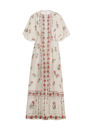 The Gesto Dress by Agua By Aguabendita is a long cream linen kaftan with wide short sleeves, featuring pink and green floral patterns and geometric borders on the front, hem, and sleeves.