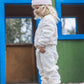 A young child in a Feather 4 Arrow Baby Girls’ and Girl’s Yummy Plush Set and a pink hat stands outside a colorful playhouse with green walls and blue trim.