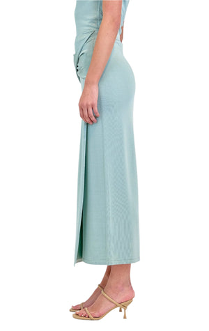 Person in profile view, wearing the Simkhai Vienna Midi Skirt in light blue, styled with beige heeled sandals, standing against a white background.