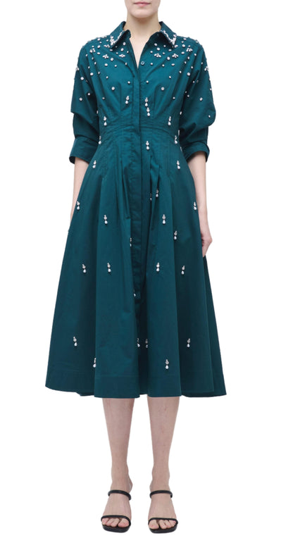 A person wearing the Simkhai Jazz Embellished Midi Dress in teal cotton poplin with white floral details, an A-line skirt, and black sandals, standing against a white background.