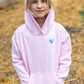 A child stands outdoors wearing the Feather 4 Arrow Girls’ Hadley Cozy Hoodie in light pink, featuring a blue heart design, with hands in pockets and looking at the camera.