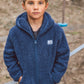 A young boy wears the Feather 4 Arrow Baby Boys’ and Boys’ Rocky Sherpa Jacket as he stands outdoors with his hands in his pockets, looking at the camera. Colorful climbing holds and a rope appear in the background, adding a playful touch to this cozy jacket’s casual style.