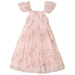 The Girls’ Clara Dress by Noralee is crafted from delicate light pink tulle and features charming puff sleeves and a smocked bodice adorned with silver sequin star and floral embellishments. Its full skirt is finished with ruffled hems, creating an enchanting tulle dress that’s perfect for special occasions.
