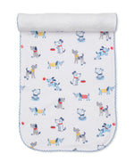 A white baby blanket with blue trim features a playful pattern of cartoon dogs in different poses—some wearing colorful collars or vests—alongside red balls and food bowls, creating an adorable design that perfectly coordinates with our Kissy Kissy Puppy Patch Burp Cloth for a cohesive nursery theme.
