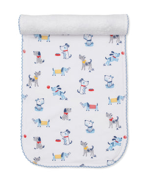 A white baby blanket with blue trim features a playful pattern of cartoon dogs in different poses—some wearing colorful collars or vests—alongside red balls and food bowls, creating an adorable design that perfectly coordinates with our Kissy Kissy Puppy Patch Burp Cloth for a cohesive nursery theme.