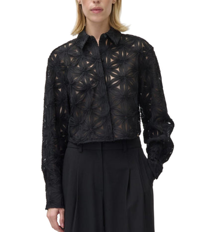 A woman wears the Simkhai Anders Shirt, a black sheer blouse with a geometric floral pattern and long sleeves, paired with high-waisted black trousers.