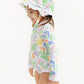 A young child stands smiling against a plain white background, wearing The Beaufort Bonnet Company’s Beaufort Swim Bucket Hat—a sun-ready accessory—paired with a matching long-sleeve, swim-ready nylon spandex swimsuit in a floral pattern.
