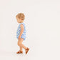 A toddler wearing The Beaufort Bonnet Company’s Baby Boys’ Broadcloth Benjamin Bubble—a blue and white striped romper—and brown sandals walks to the left against a plain white background.