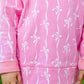 A child is standing outdoors, wearing The Beaufort Bonnet Company Baby Girls’ and Girls’ French Terry Cassidy Comfy Crewneck in pink with a charming bow print. Only the torso and hands are visible.