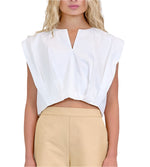 Model wears the Simkhai Wrenli Pleated Top, a sleeveless white V-neck blouse with a pleated front, paired with high-waisted beige pants; shown from the waist up.