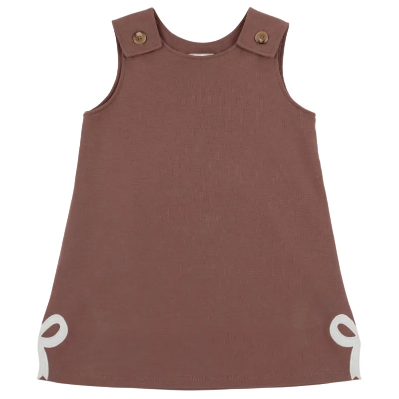 Sleeveless brown Girls’ Juliet Jumper toddler dress from The Beaufort Bonnet Company, crafted from soft Pima Cotton Knit with buttoned shoulder straps and white bow accents at the bottom corners, laid flat against a white background—a charming piece for little ones.