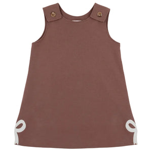 Sleeveless brown Girls’ Juliet Jumper toddler dress from The Beaufort Bonnet Company, crafted from soft Pima Cotton Knit with buttoned shoulder straps and white bow accents at the bottom corners, laid flat against a white background—a charming piece for little ones.