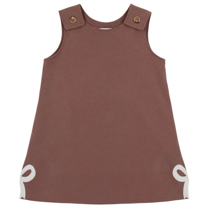 Sleeveless brown Girls’ Juliet Jumper toddler dress from The Beaufort Bonnet Company, crafted from soft Pima Cotton Knit with buttoned shoulder straps and white bow accents at the bottom corners, laid flat against a white background—a charming piece for little ones.
