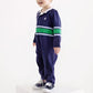 A young child wearing The Beaufort Bonnet Company’s Baby Boys’ Sir Proper’s Rugby Romper—navy blue with green and white stripes—stands smiling on a white pedestal against a plain white background.