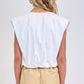 A person stands with their back to the camera, wearing the Simkhai Wrenli Pleated Top in white and beige high-waisted shorts against a plain background.